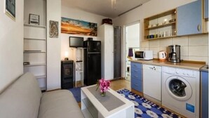 A compact living space with a sofa, a flat-screen TV, a refrigerator, a microwave, a coffee maker, and a washing machine. - Apartments Carpe Diem (Vir)