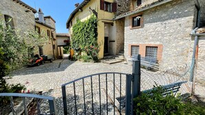 A cobblestone courtyard with stone buildings, a metal gate, and a bench.