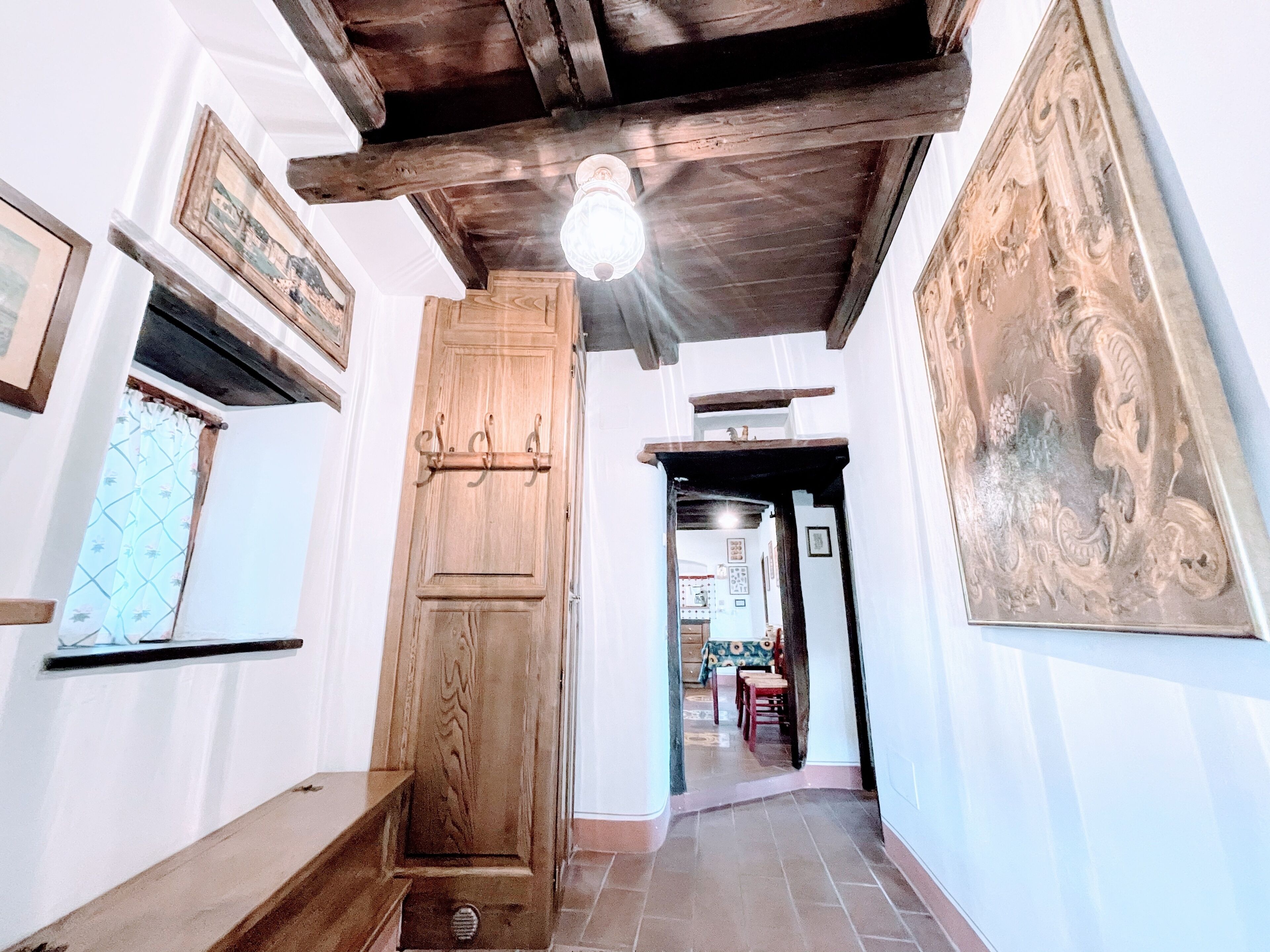 A hallway with a wooden door, a ceiling light, and a dining area in the background.
