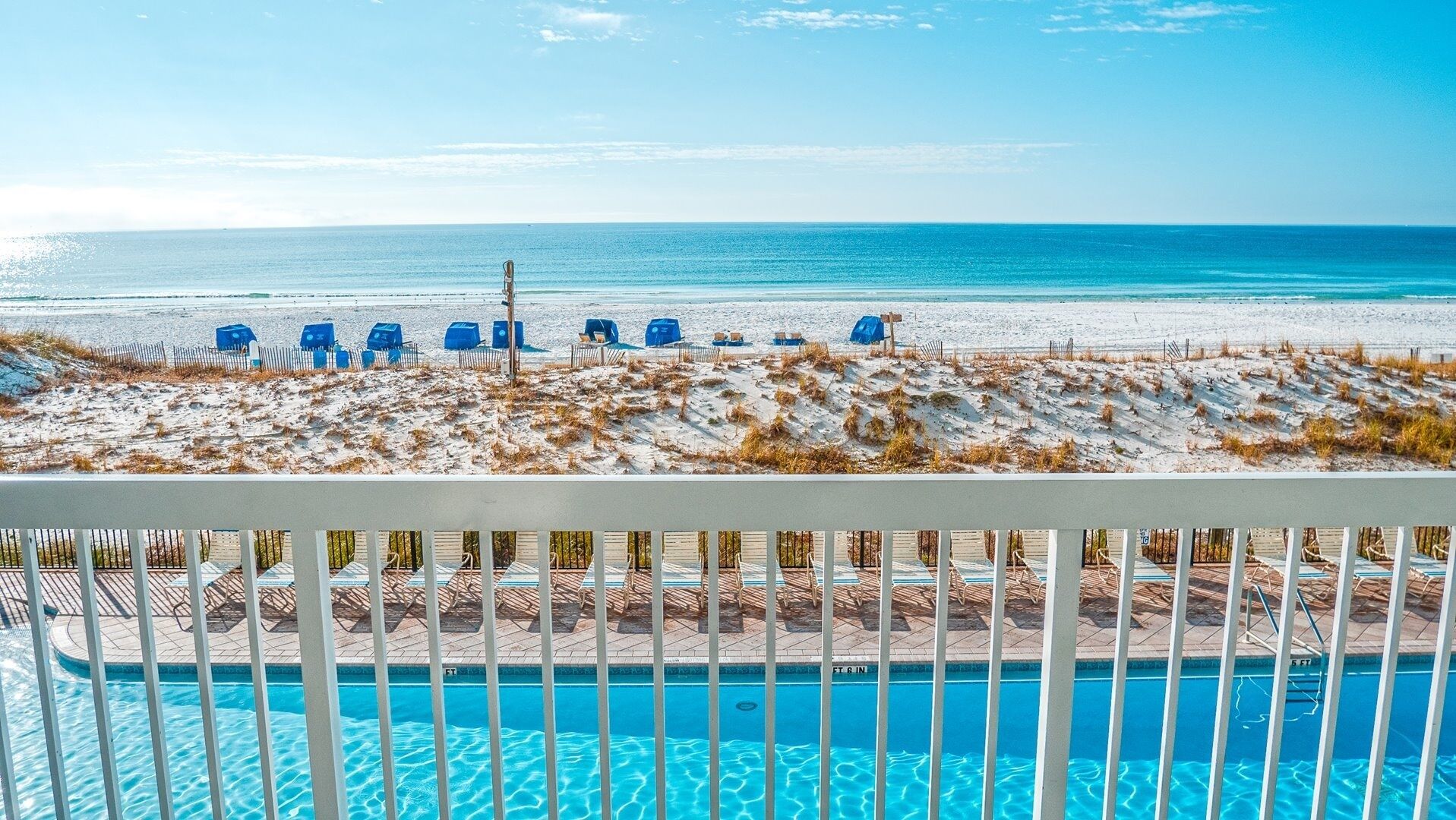 A poolside view with a beach and ocean in the background.