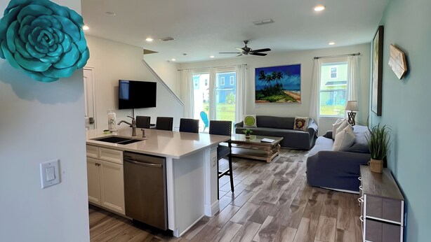 A modern kitchen with a central island, a dining area with chairs, a living room with a sofa, and a large window. - Villa in Margaritaville-Near Disney-Universal-SeaWorld-H20 (Kissimmee)