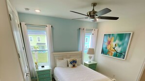 A bedroom with a bed, a ceiling fan, a window with curtains, a nightstand, a lamp, and a painting on the wall. - Villa in Margaritaville-Near Disney-Universal-SeaWorld-H20 (Kissimmee)