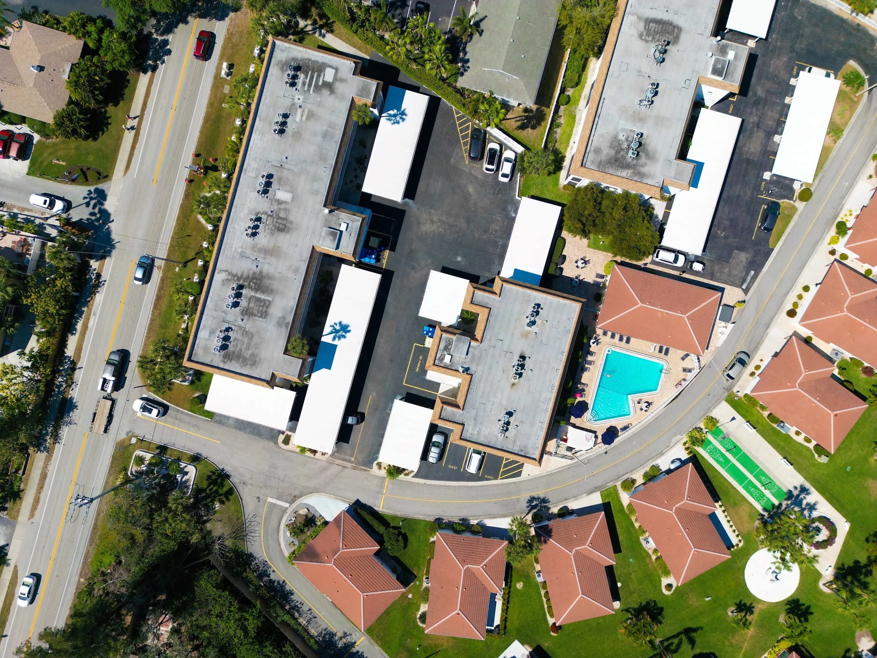 An aerial view of a commercial complex with multiple buildings, parking areas, and a swimming pool.