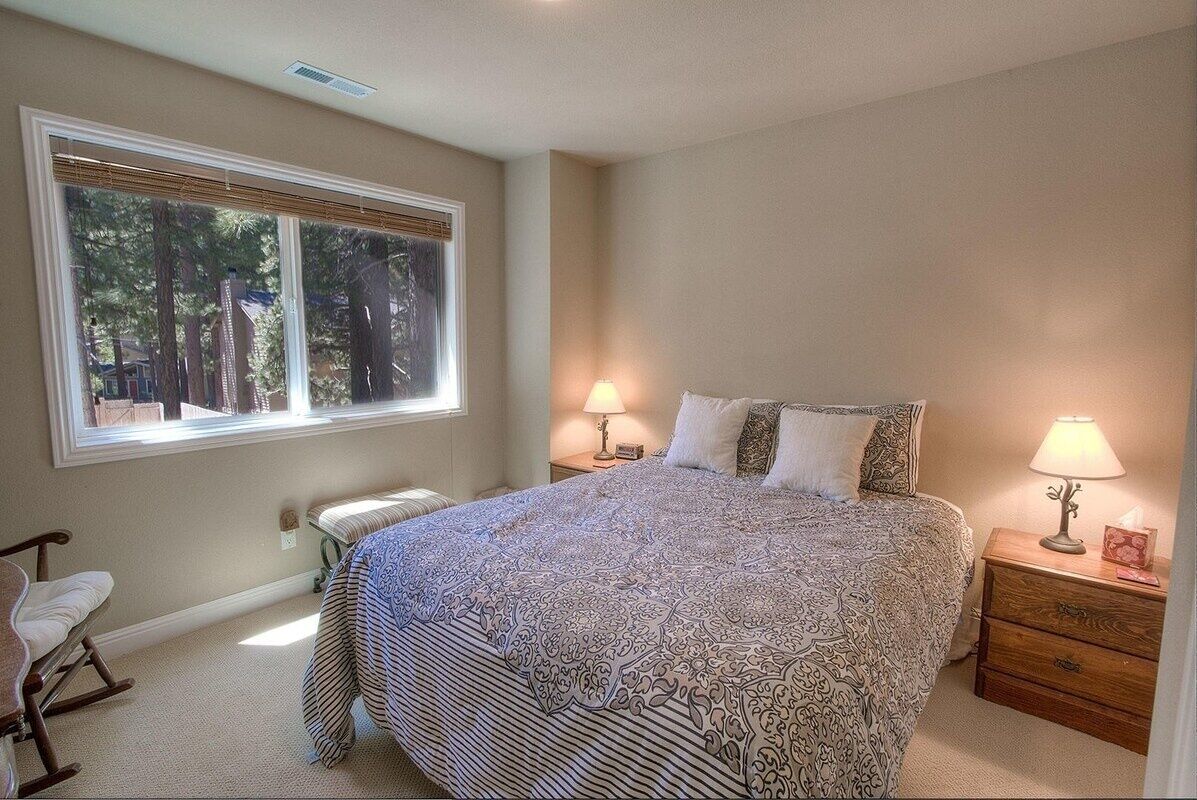 A bedroom with a large bed, two bedside tables with lamps, a rocking chair, and a window with blinds.