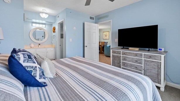 A bedroom with a bed, a ceiling fan, a television, and a dresser. - Terrace at Pelican Beach 1005 2 Bedroom Condo by Pelican Beach Management (Destin)