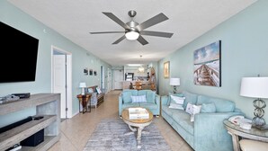 A living room with a TV, a ceiling fan, a coffee table, and a sofa. - Terrace at Pelican Beach 1005 2 Bedroom Condo by Pelican Beach Management (Destin)