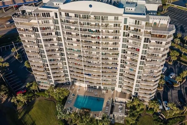 A multi-story hotel with balconies, a swimming pool, and a parking area.