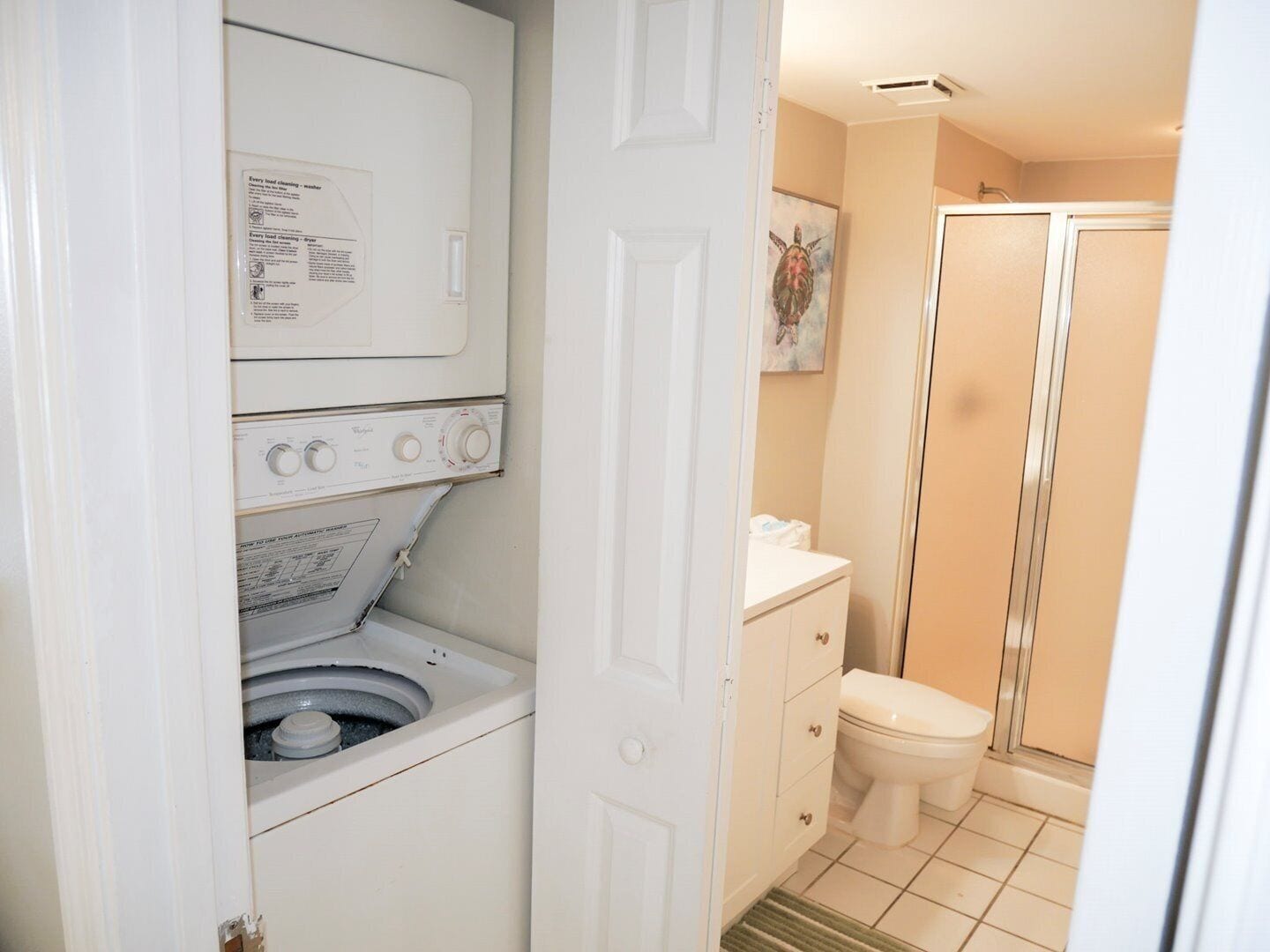 A compact laundry area with a washing machine and dryer, a small bathroom with a toilet and shower, and a cabinet with drawers.