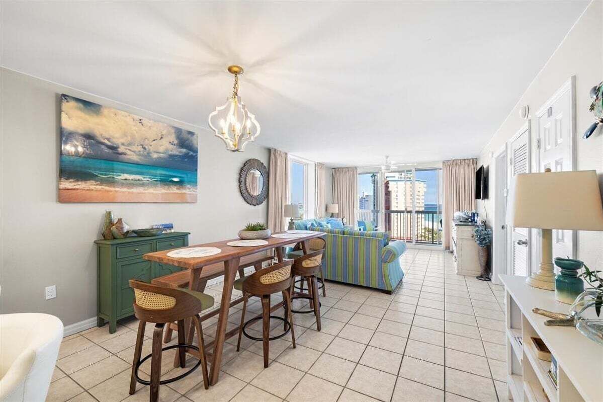 Een moderne woonkamer met een eethoek, een groot schilderij van een strandgezicht en uitzicht op de stad door grote ramen.
