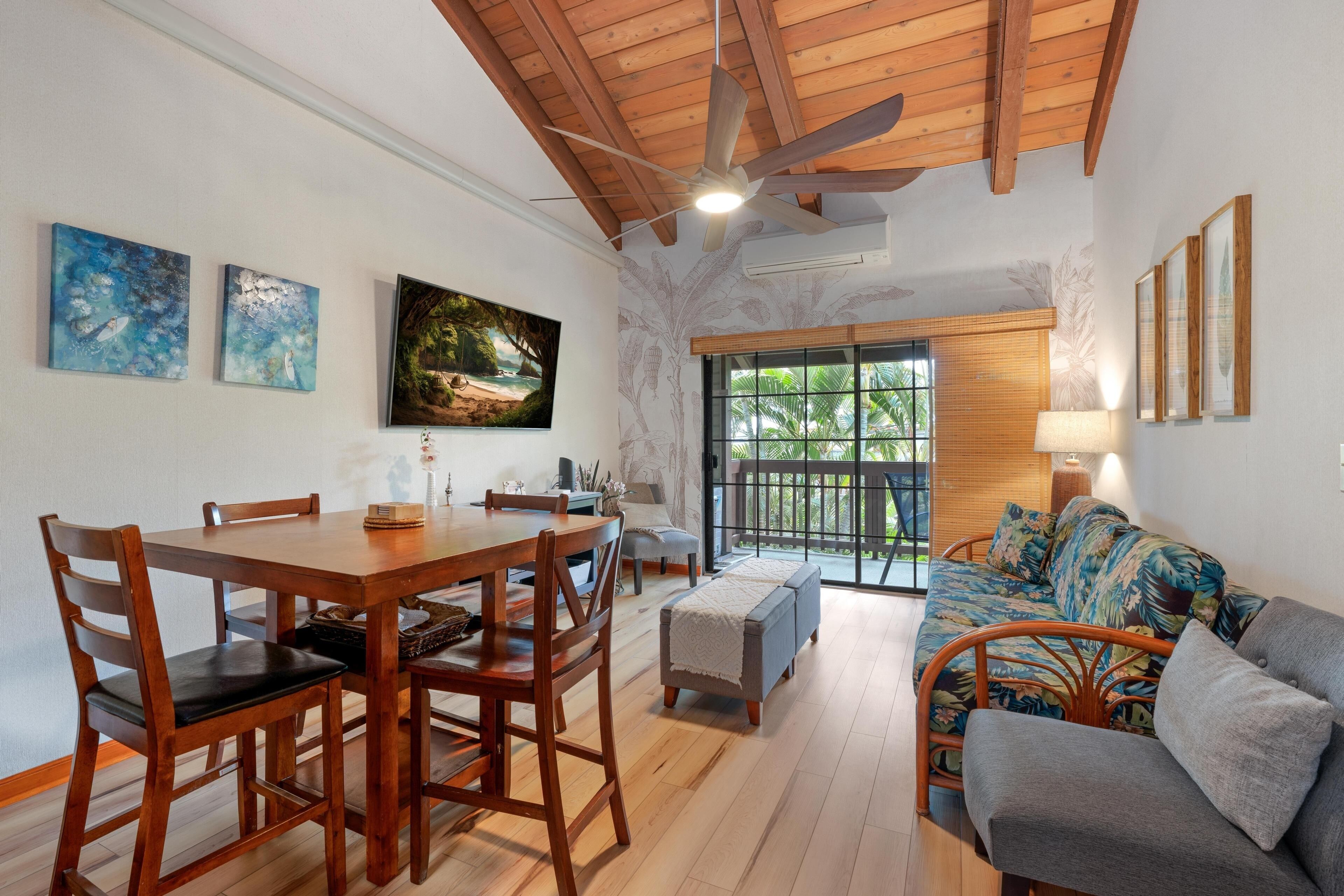 A dining area with a wooden table and chairs, a sofa with a tropical print, and a ceiling fan.