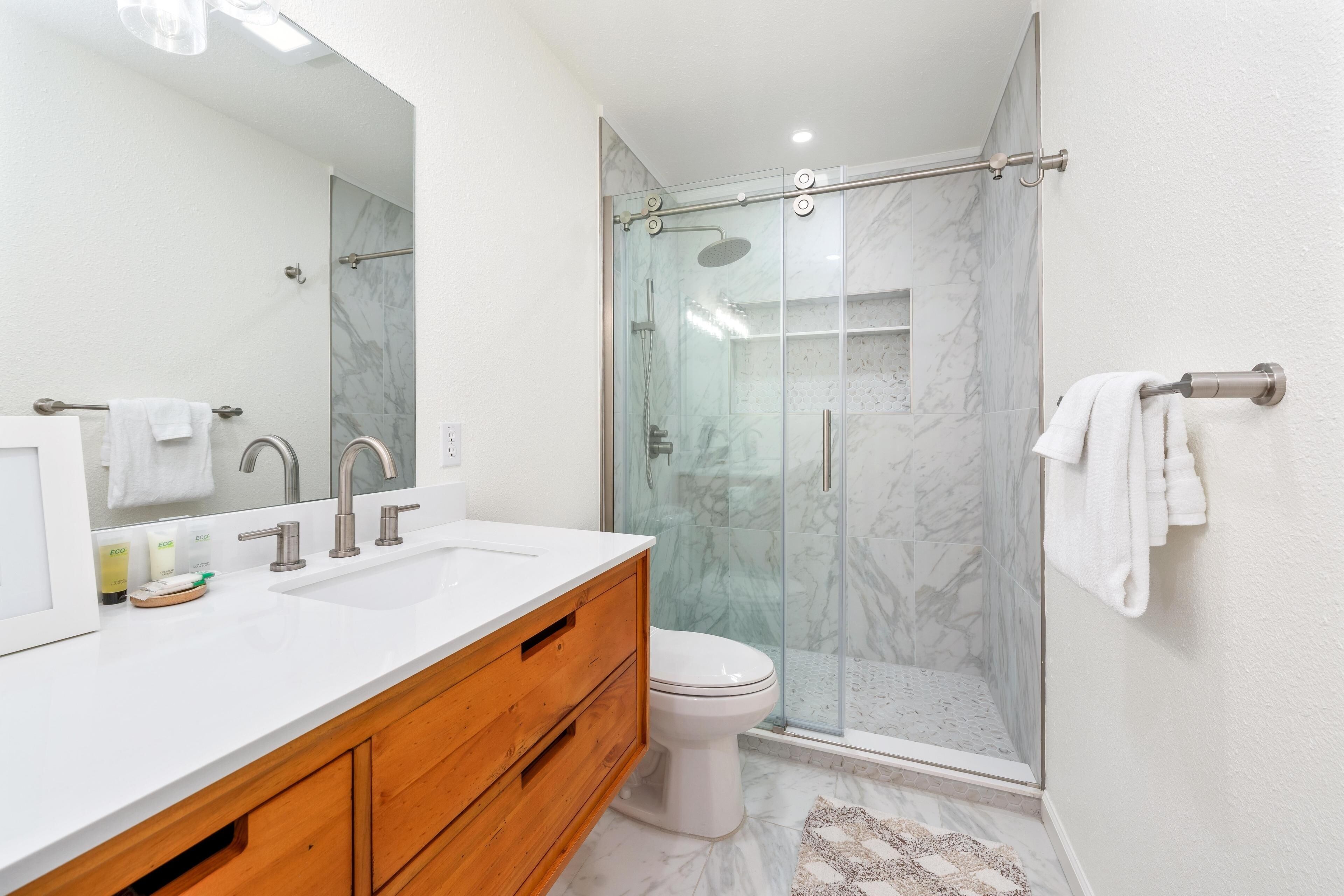 A modern bathroom with a white sink, wooden vanity, and a glass-enclosed shower.