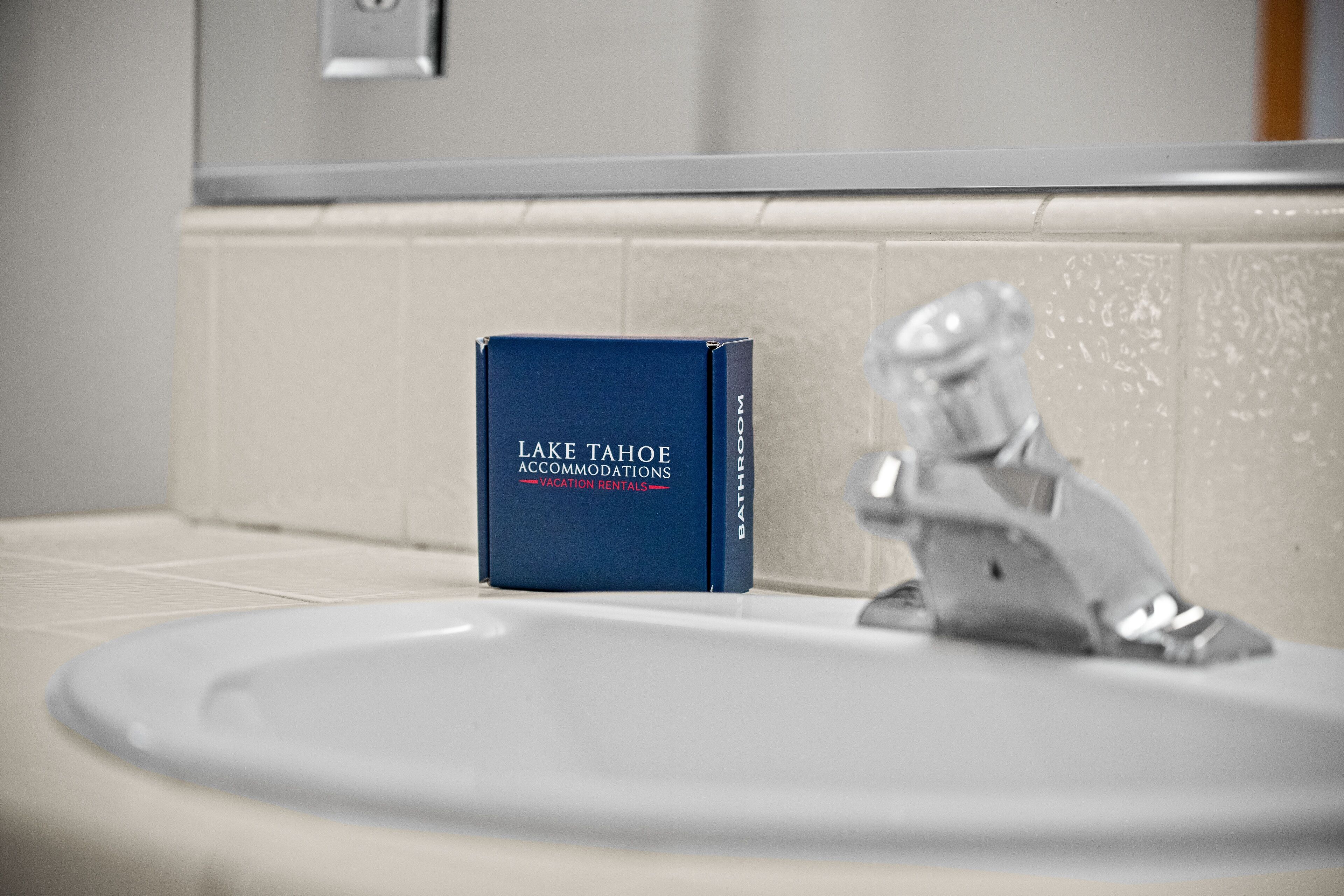 A bathroom with a white sink, a mirror, and a blue box labeled "Lake Tahoe Accommodations Vacation Rentals."