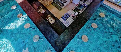 A pool with a unique geometric design, a bar area with stools and a counter, and a stone wall.