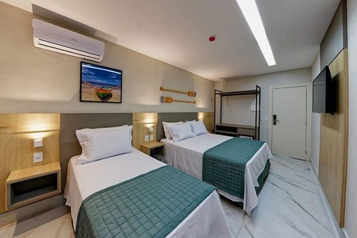 A hotel room with two beds, a TV, an air conditioning unit, and a painting on the wall.