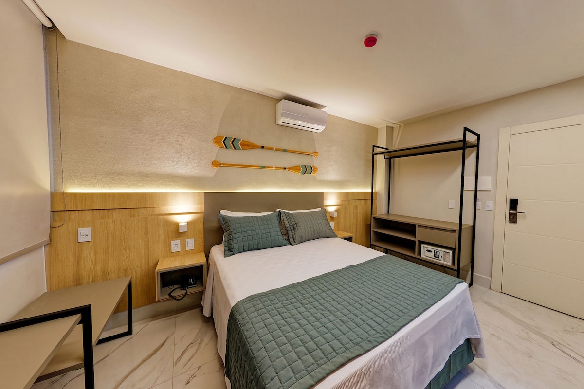 A hotel room with a bed, bedside tables, a wall-mounted air conditioner, and a TV.