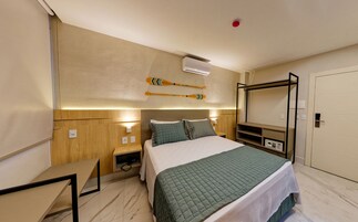 Una habitación de hotel con cama, mesitas de noche, aire acondicionado instalado en la pared y televisor.