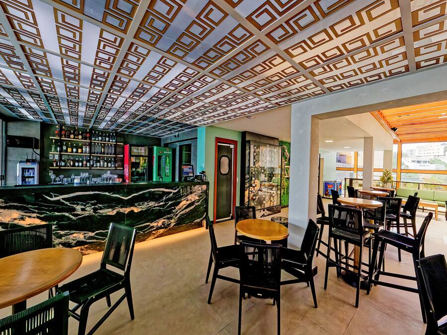 Un espace bar moderne doté d’un comptoir en marbre, de nombreux sièges et d’un plafond orné de motifs.