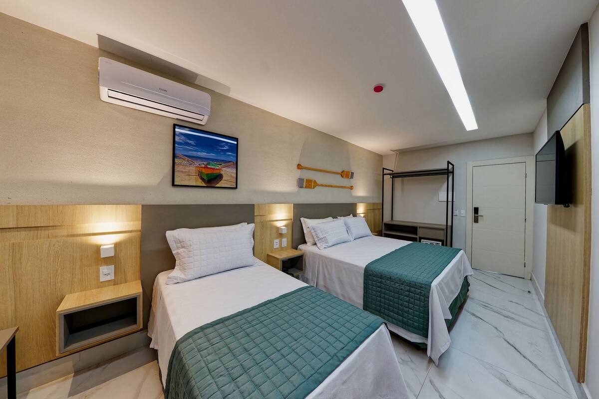 A hotel room with two beds, a TV, a painting, and an air conditioning unit.