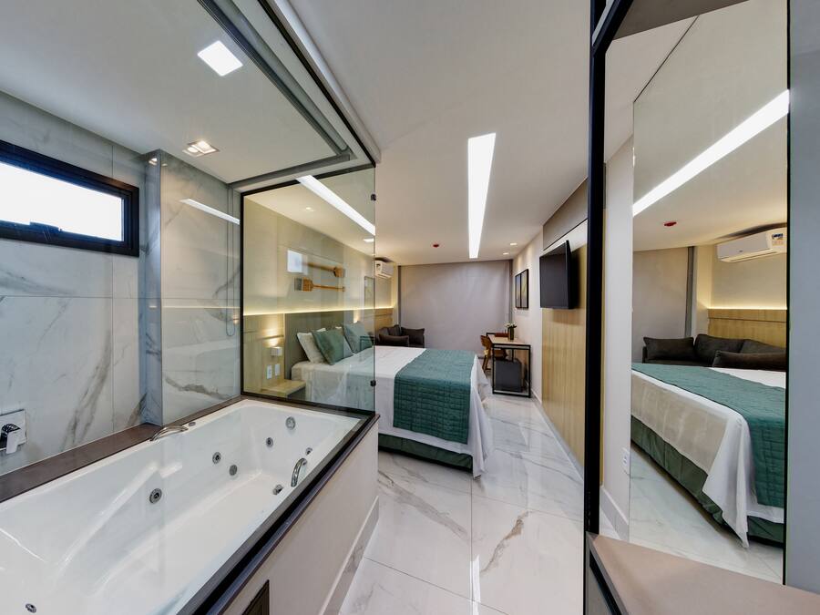 Una habitación de hotel moderna con un espejo grande, una bañera, una cama con ropa de cama verde y un pequeño escritorio.