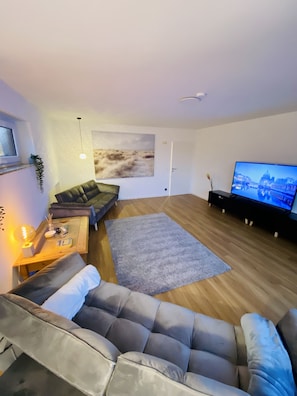 A modern living room with a grey sofa, a wooden coffee table, a grey rug, and a flat-screen TV on a stand. - Apartment Steinhude. 115sqm + 30sqm loggia between bathing island and promenade (Wunstorf)