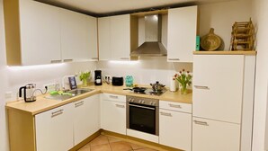 A compact kitchen with white cabinets, a stove, a sink, and a coffee maker.