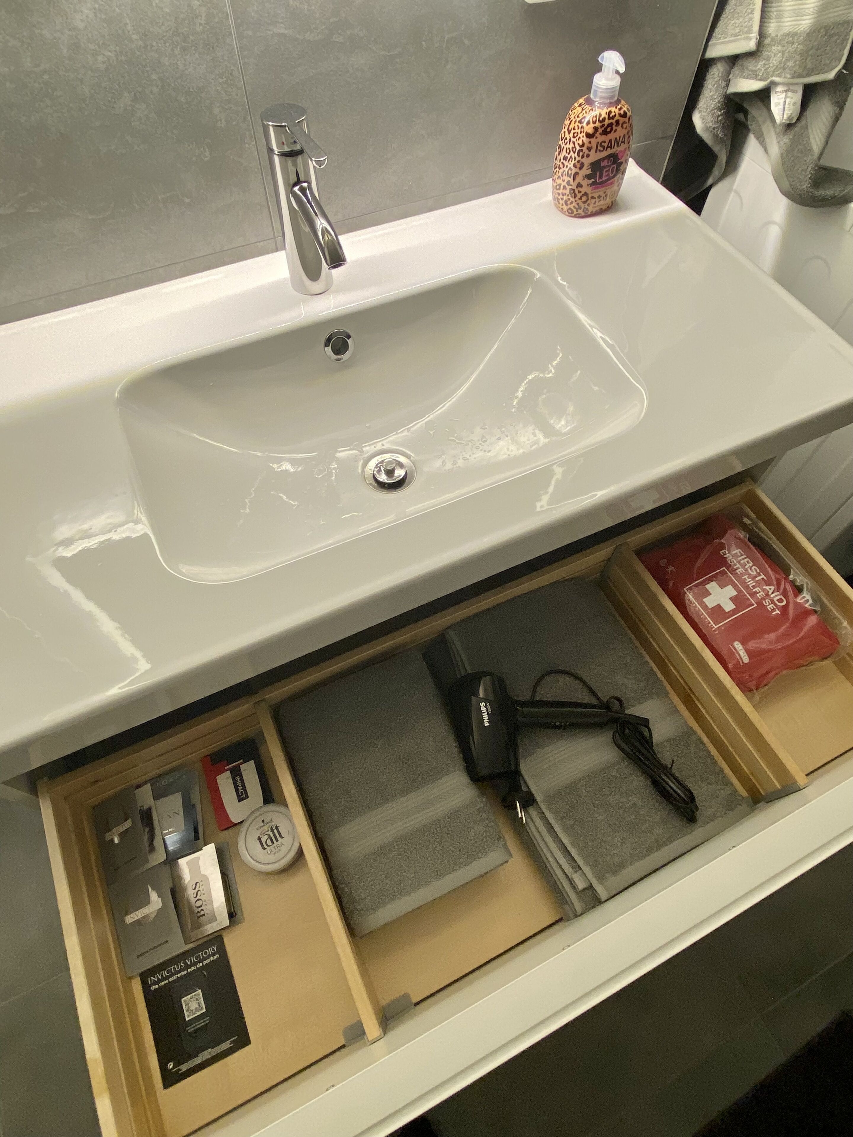 A bathroom sink with a mirror above it, a bottle of hand soap, and a first aid kit drawer below.