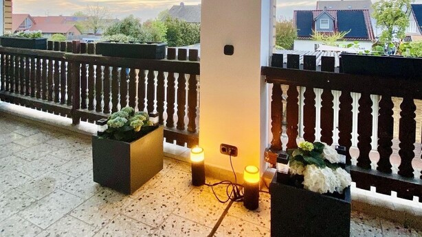 A covered outdoor area with a wooden ceiling, a white pillar with a light fixture, and a railing with potted plants.