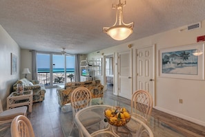 Relax in this spacious living area with a sofa, chairs, and dining table, offering a view of the ocean through large sliding glass doors.