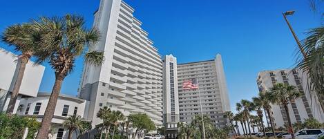 A modern hotel with a prominent American flag, surrounded by palm trees and a clear blue sky.