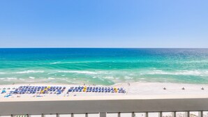 Ein Strand mit klarem türkisblauem Wasser und einem weißen Sandstrand. Es gibt Reihen aus blauen und gelben Strandsonnenkappen und Liegestühlen.