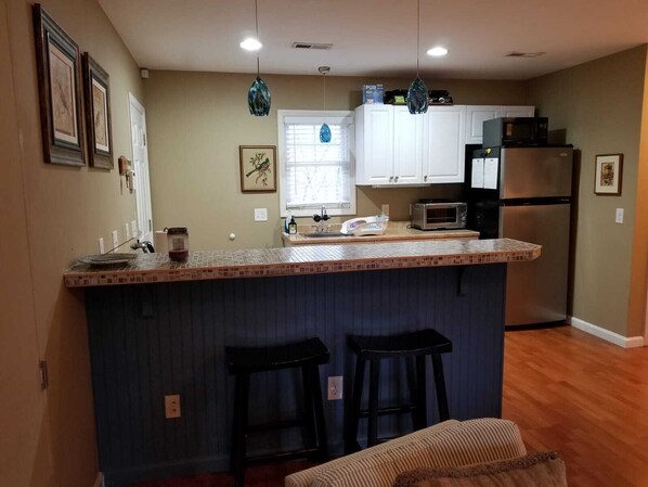 A kitchen with a central island, bar stools, a microwave, a refrigerator, and a window with blinds.