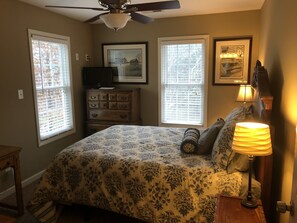 A bedroom with a bed, dresser, ceiling fan, and two windows with blinds.