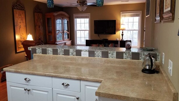 A kitchen with a tiled backsplash, white cabinets, a ceiling fan, and a television. - Leafy, Suburban Abode (Greensboro)