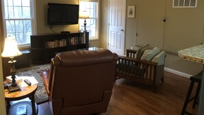 A living room with a leather chair, a bookshelf, a television, and a crib. - Leafy, Suburban Abode (Greensboro)