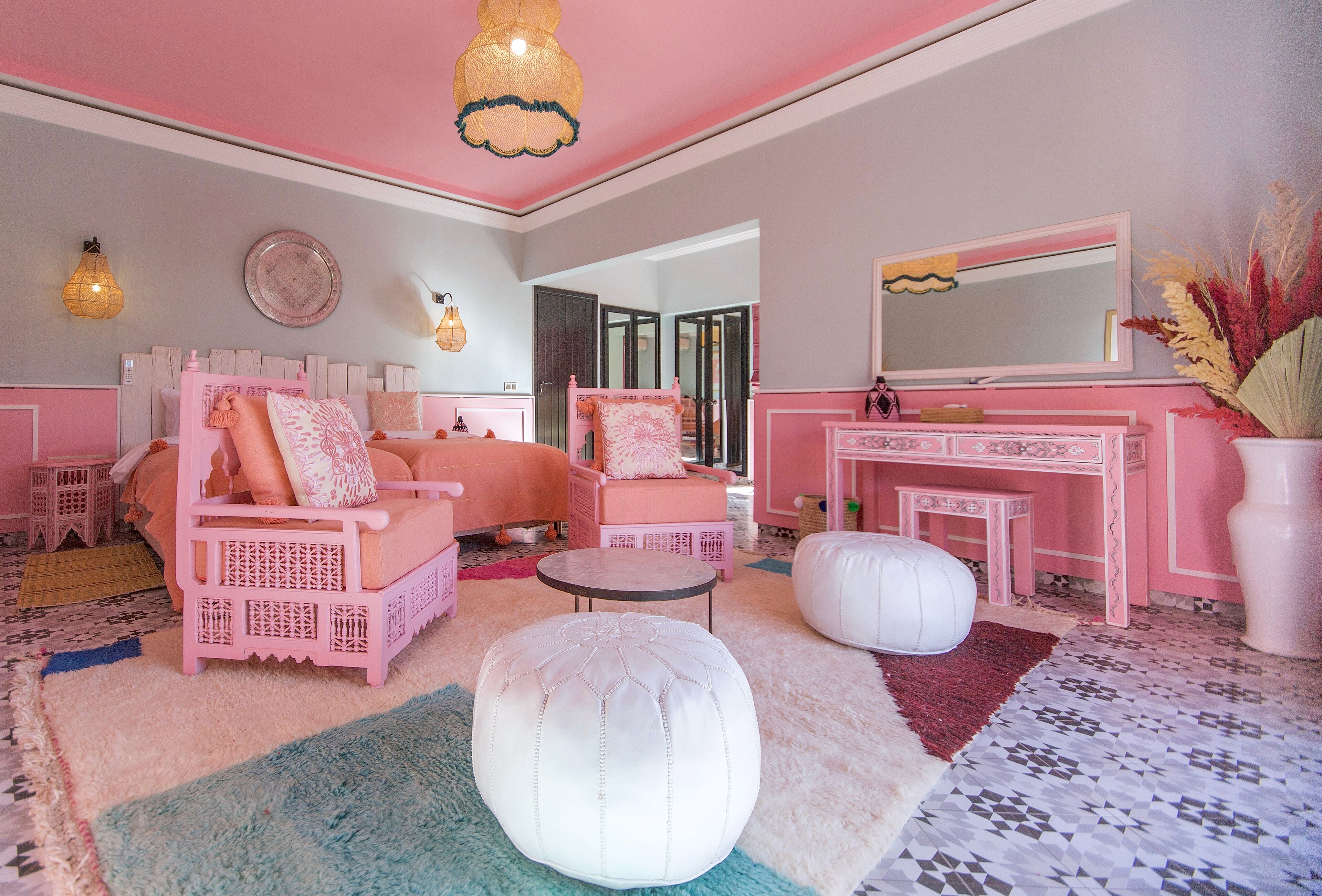 Slaapkamer in roze tinten met een bed, twee stoelen, een klein tafeltje en een grote poef.