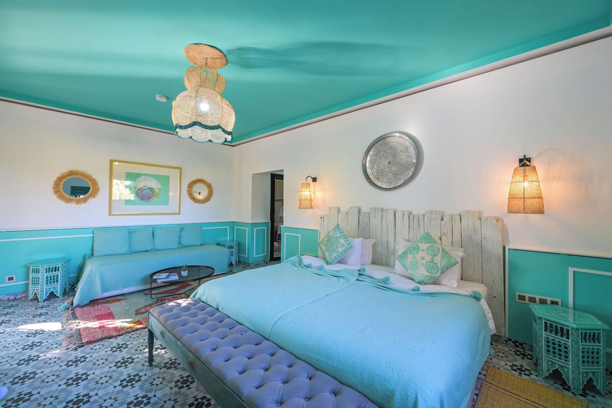 A room with a bed, a bench, a small table, and a wall-mounted light fixture.