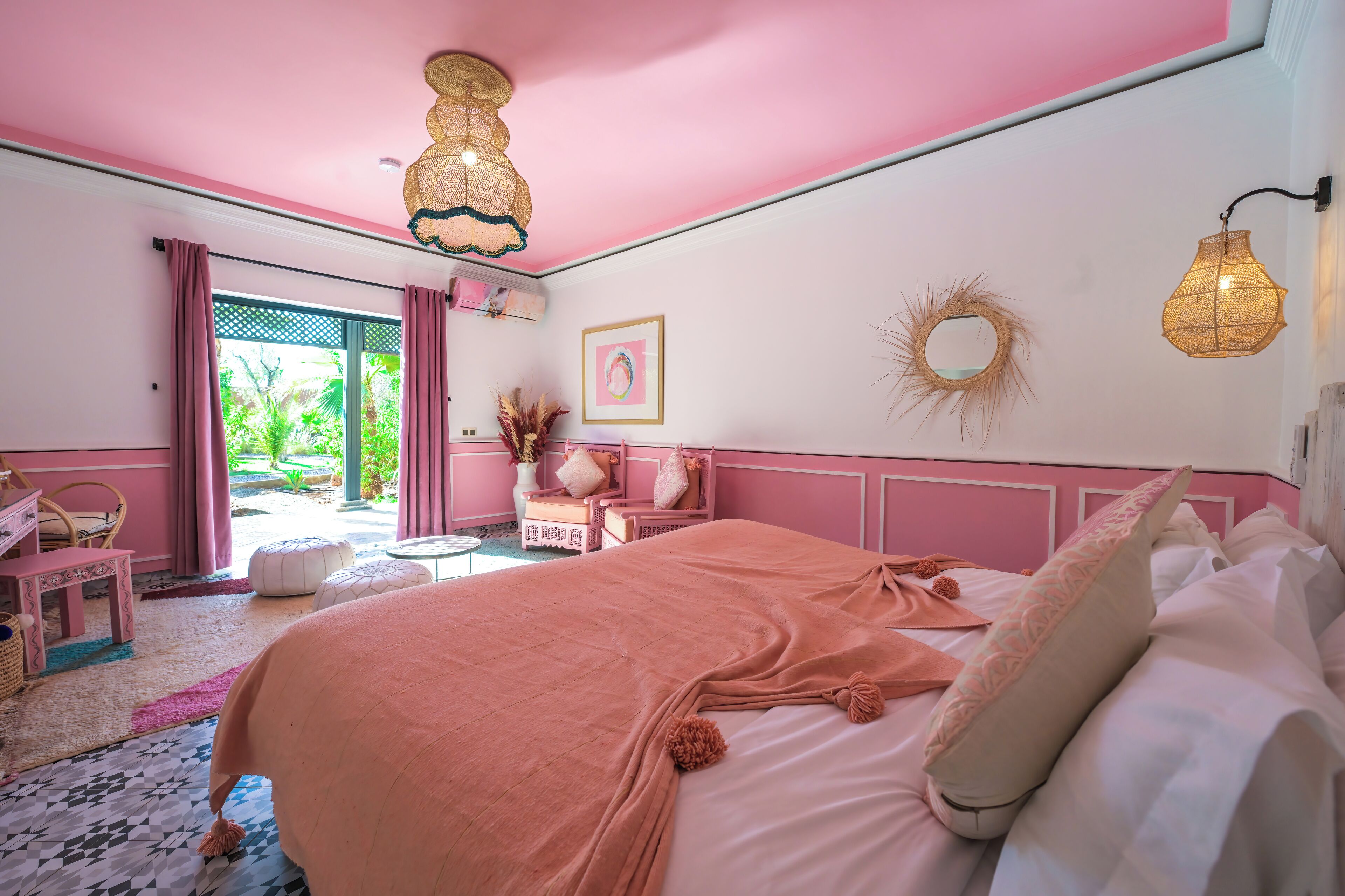 A pink-themed bedroom with a bed, pillows, and a hanging light fixture.