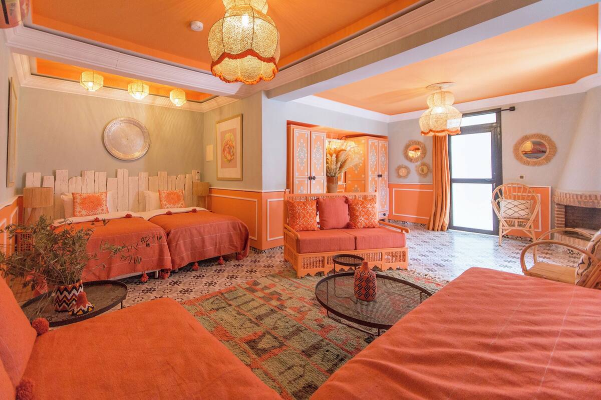 A room with two beds, a sofa, a small table, and a chair. There are decorative pillows and a vase on the sofa.