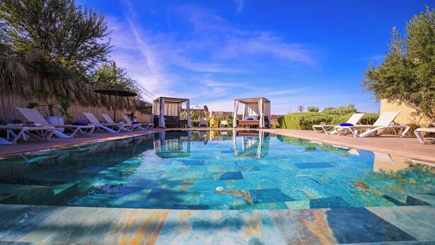 A swimming pool with lounge chairs and canopies, surrounded by trees and a clear sky. - Maison Daouia (Marrakech)