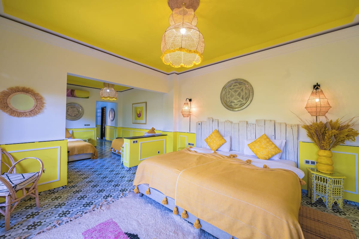 A room with a bed, a chair, a small table, a lamp, and a decorative wall piece.