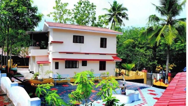 A two-story building with a red roof and white walls, surrounded by lush greenery and palm trees. - Holy Trinity - Serviced Villa (Kundara)