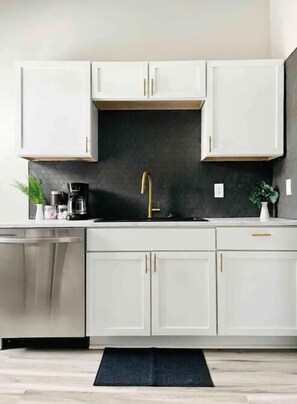 Una cocina moderna con armarios blancos, salpicadero negro y grifo dorado.