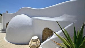 A white, curved architectural feature with a stone base, a small white object, and green plants. - Paraga Scorpios Villa 2 7mins Walk to Beach by Calypso Sunset Villas (Mykonos)