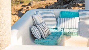 A stone balustrade overlooking a coastal view with a white cushioned seating area with striped and solid pillows. - Paraga Scorpios Villa 2 7mins Walk to Beach by Calypso Sunset Villas (Mykonos)