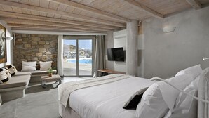 A bedroom with a large bed, a TV, and a stone wall. - Paraga Scorpios Villa 2 7mins Walk to Beach by Calypso Sunset Villas (Mykonos)