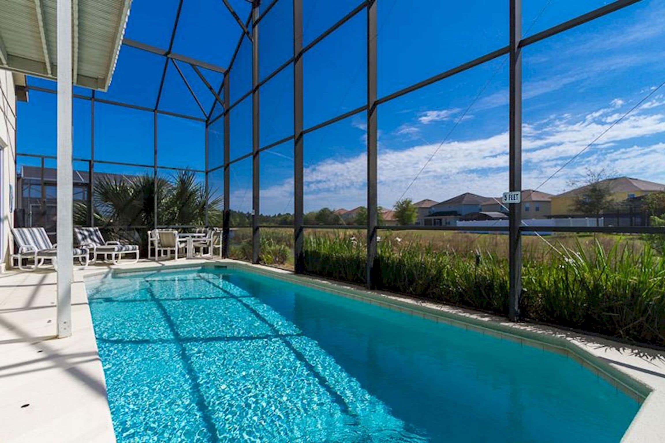 A swimming pool with clear blue water, surrounded by a glass enclosure, and a view of houses in the background.