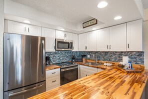 A modern kitchen with stainless steel appliances, white cabinets, and a wooden countertop. - Papakea L207 Ocean Front 1 Bedroom 1 Condo by RedAwning (Lahaina)