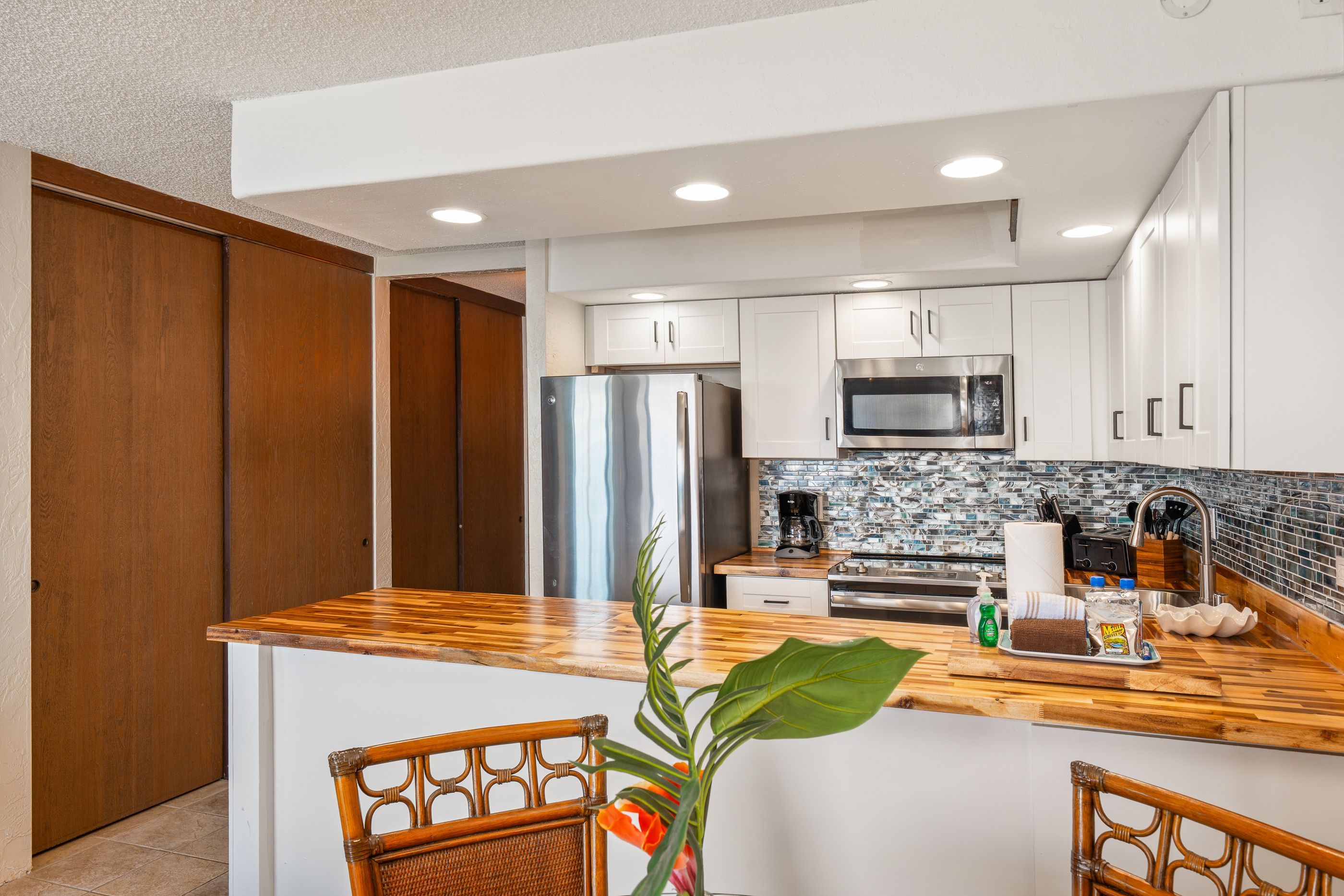 A modern kitchen with white cabinets, stainless steel appliances, a wooden countertop, and a large island with seating.