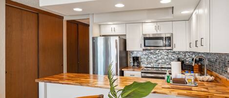 A modern kitchen with white cabinets, stainless steel appliances, a wooden countertop, and a large island with seating.