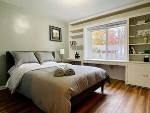 Une chambre à coucher avec un lit, des étagères intégrées, une fenêtre et un tableau au mur.